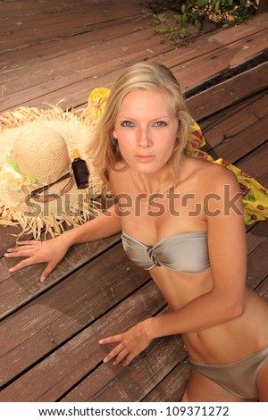 Beauty portrait of woman laying on wooden floor with straw hat sunglasses and suntan oil