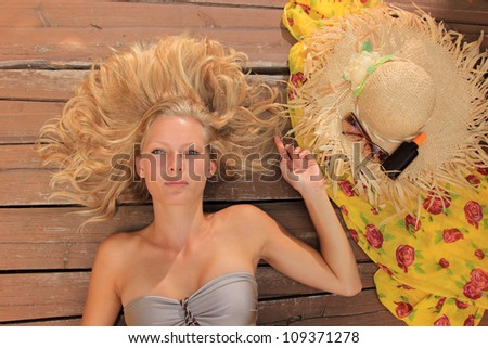 Beauty portrait of woman laying on wooden floor with straw hat sunglasses and suntan oil