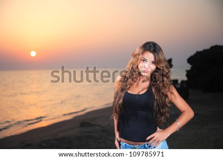 Beautiful young sexy fashion model in jeans by the sea at sunrise