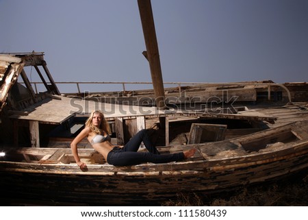 portrait of sexy blond woman in jeans posing in from of shipwreck