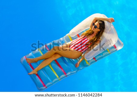 amazing beautiful girl in bikini on an  air mattress swims in the pool of a luxury hotel, summer vacation.