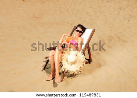 Young beautiful woman with cocktail on sunbed on the beach