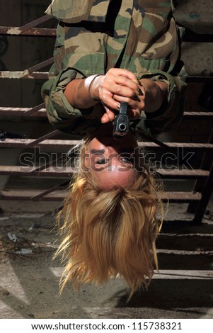 Beautiful sexy blond woman with gun hanging upside down
