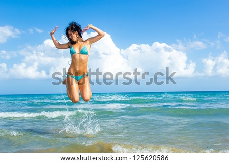 Beautiful young woman in bikini on the beach jumping in the water