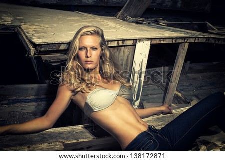portrait of sexy blond woman posing in front of an old wooden ship wreck