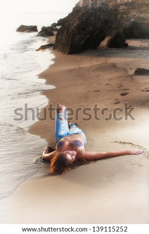 Beautiful young woman in bikini top and jeans on the beach