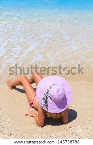 Woman laying on the beach in beach pink straw hat enjoying summer holidays looking at the ocean