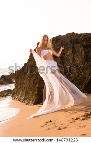 Woman wrapped in wedding veil on the beach at sunset