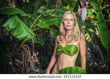 Young blonde woman posing with banana tree leaves