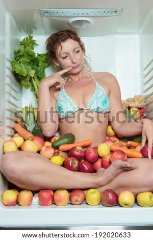 Woman sitting in a fridge in the lotus position surrounded by fruits making faces