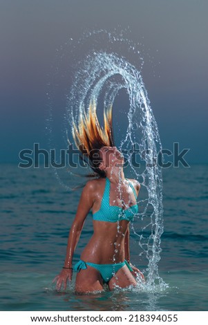 Woman splashing water with her hair in the ocean at night