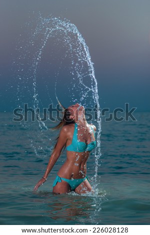 Woman splashing water with her hair in the ocean at night