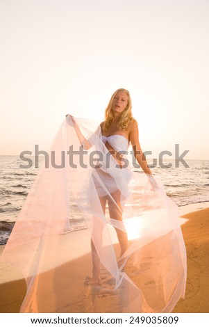 blonde woman wrapped in wedding veil on the beach
