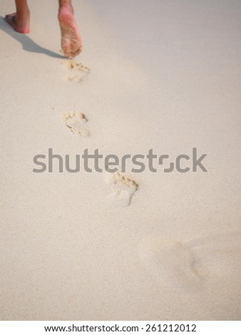 woman walking on sand beach leaving footprints in the sand. Closeup detail of female feet and golden sand