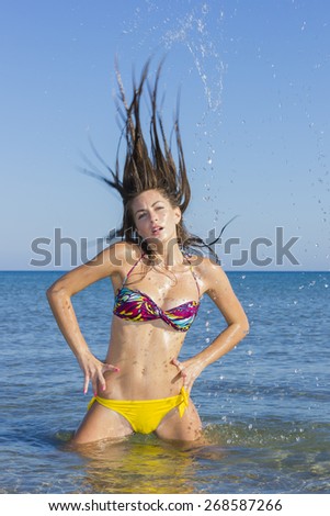 Beautiful young woman in bikini on the beach splashing water