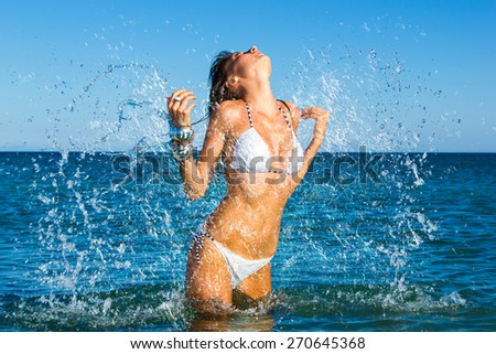 Beautiful young woman in bikini on the beach splashing water all over