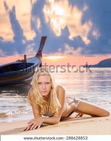Beautiful young blonde woman in bikini laying on the beach at sunset with lon tail boat on background