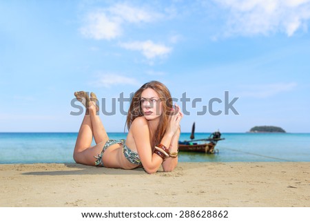 Beautiful young woman in bikini laying on the beach with lon tail boat on background