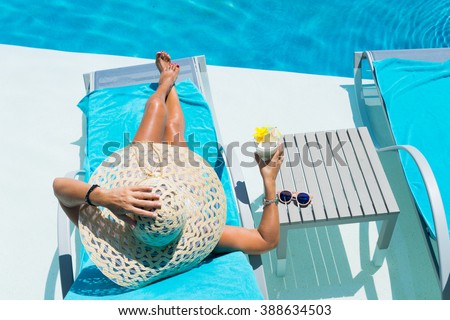 Woman in hat relaxing at the poolside with pina colada cocktail
