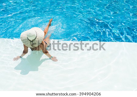 beautiful woman in a hat sitting on the edge of the swimming pool