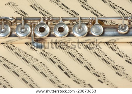 Silver flute instrument resting on an old faded music score