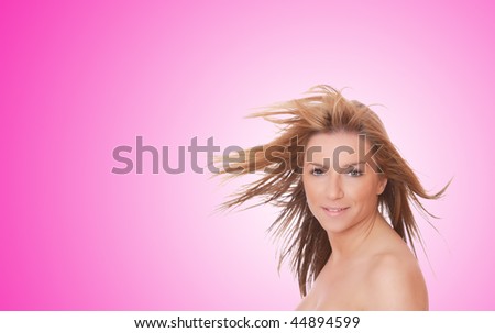 A beautiful young woman with her hair blowing in front of a pink background