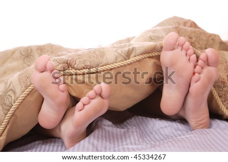 View of a couple\'s feet sticking out of the bed sheet while in bed