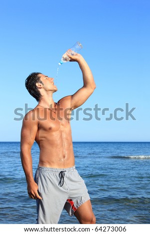 sexy caucasian fit man posing at the  beach - drinking water