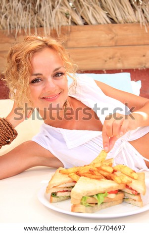 Beautiful young woman by the sea in Greece eating club sandwich