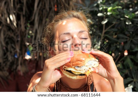 Woman with big round eyes eating a yummy cheeseburger