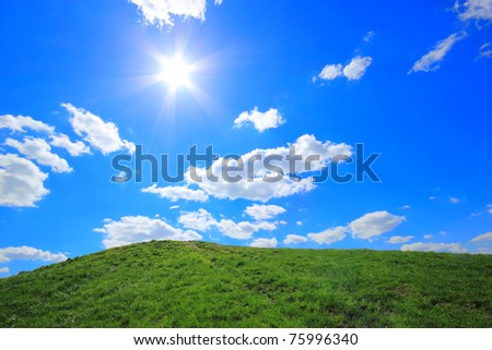 Green grass hills under midday sun in blue sky.
