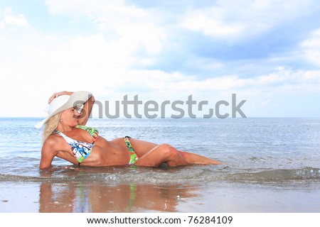 Sexy and fit blond woman wearing a hat  laying on the beach