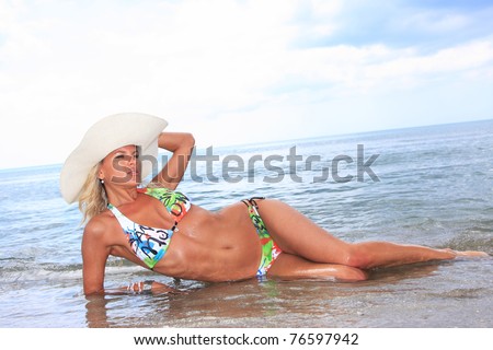 Sexy and fit blond woman wearing a hat  laying on the beach