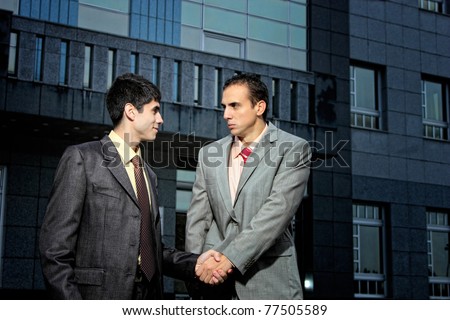 two Handsome  Businessman standing shaking hands in front of corporate