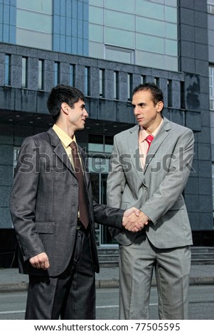 two Handsome  Businessman standing shaking hands in front of corporate