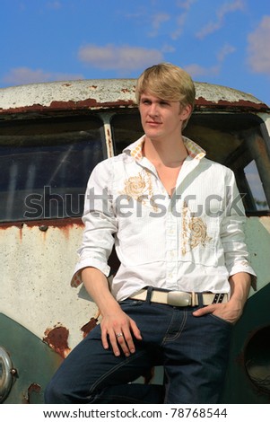Handsome young man posing at a  old broken car in a field