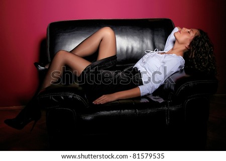Young woman in black skirt and white dress sitting on black sofa