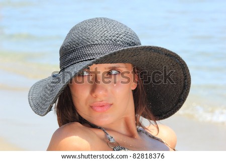 Young beautiful sexy tanned woman in hat and bikini laying on sea beach