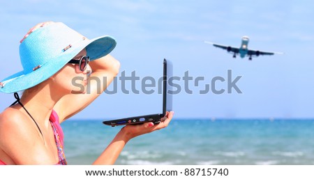 Young sexy woman Relaxing on the beach with her laptop and an airplane passing behind her - Travel concept