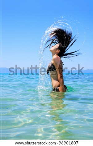 Young beautiful tanned woman in bikini in the sea splashing water with her hair
