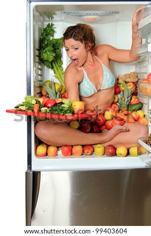 Woman sitting in a fridge in the lotus position surrounded by fruits holding a cutting board with cut apples