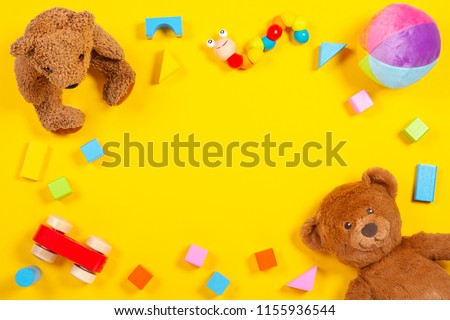 Baby kids toys frame with teddy bear, wooden toy car, colorful bricks on yellow background. Top view
