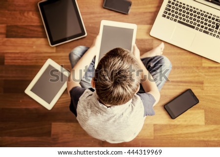 Little boy using tablet PC sitting on wooden floor. Digital tablets, laptop, mobile phones all around. Selective focus. Toned image. Top view. Education, learning, technology concept