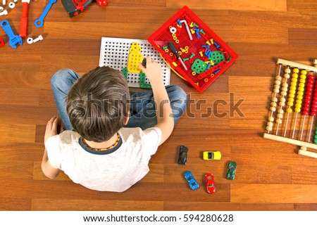 Little kid playing with toys tool kit while sitting on the floor in his room. Top view