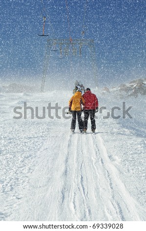 T bar ski lift pulling couple of skiers up the slope. Snowy winter in European Alps.