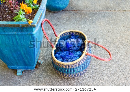 Woven basket with blue wool and yarn next to a large ceramic planter with flowers