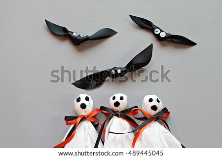Halloween concept background : Three halloween ghosts DIY made from white tissue paper, black and orange ribbon and three bats DIY made form black ribbon on gray background