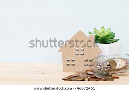 Business, finance, saving money, property ladder or mortgage loan concept : Wood house model, coins scattered from glass jar on desk table