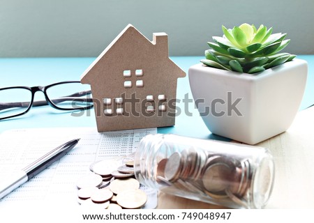 Business, finance, saving money, property ladder or mortgage loan concept : Wood house model, coins and financial statement or saving account book on desk table