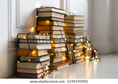 Decoration of the house in Scandinavian style. Stacks of books on the floor with a glowing garland. Christmas decor. Background for Christmas card. Soft focus